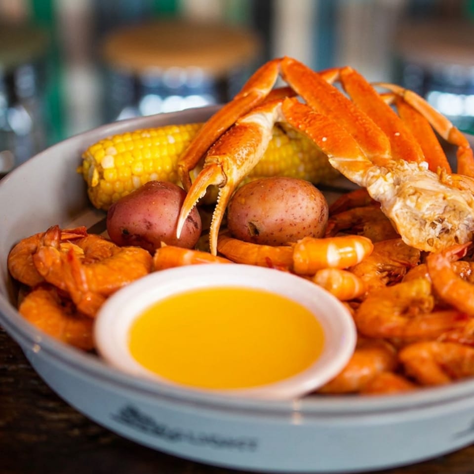 Seafood boil platter with crab legs, shrimp, corn, red potatoes, and dipping sauce on a restaurant table.