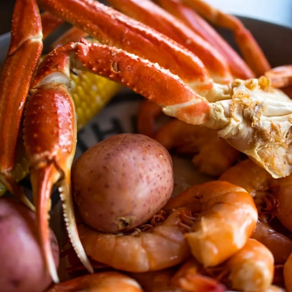 Seafood boil platter with crab legs, shrimp, corn on the cob, red potatoes, and sausage.