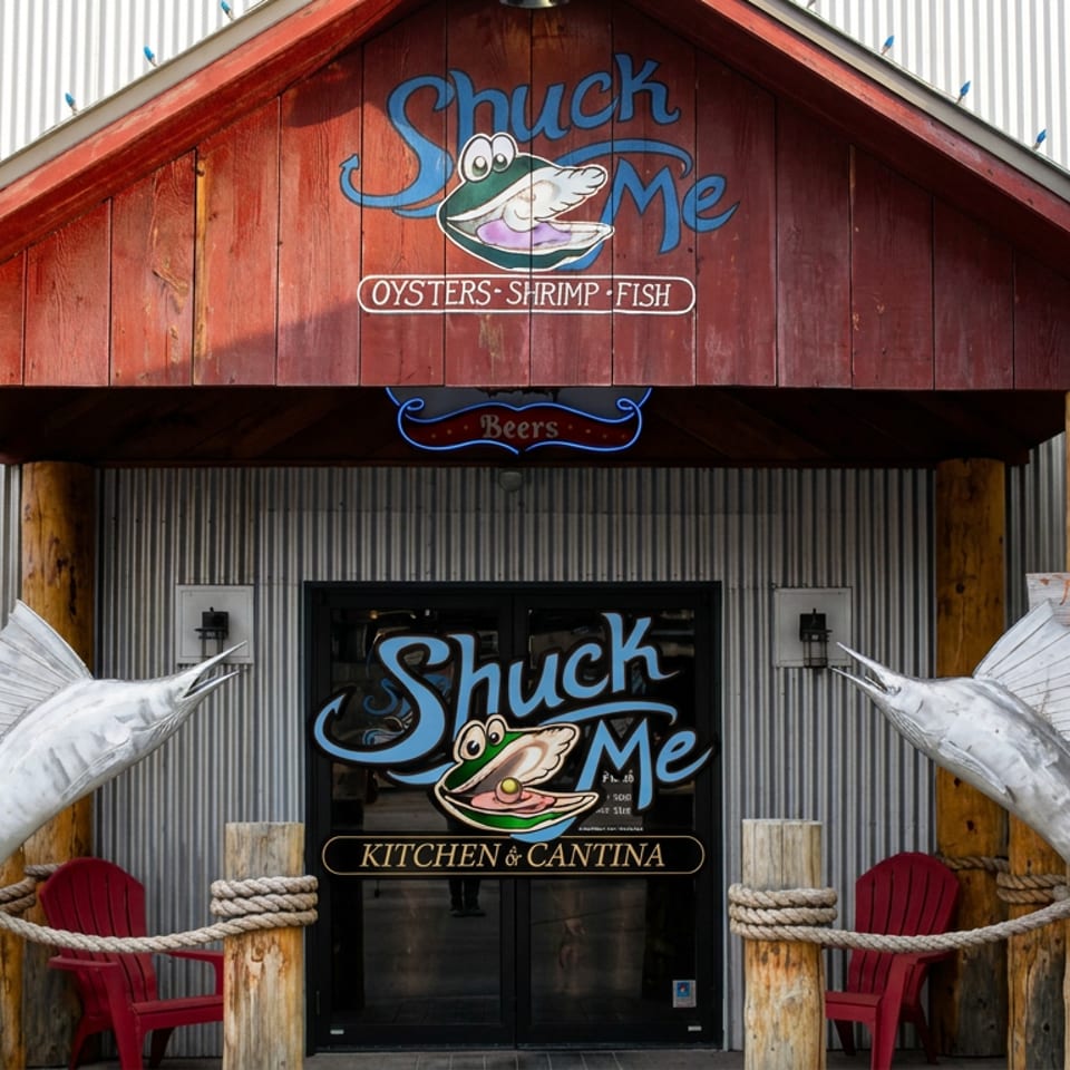 Chuck Me seafood restaurant entrance featuring large fish sculptures, rustic wooden posts, red chairs, and oyster, shrimp, and fish signage.